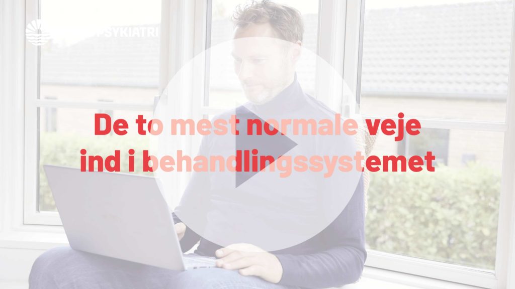 Mand sidder ved et vindue med en bærbar computer på skødet, stor play-knap og rød tekst over billedet.