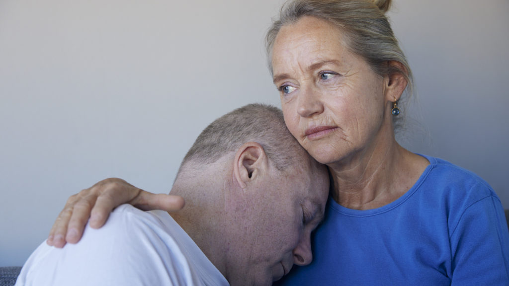 kvinde holder en mand tæt, mens hun ser eftertænksom ud. De udstråler omsorg og trøst i et følelsesladet øjeblik.