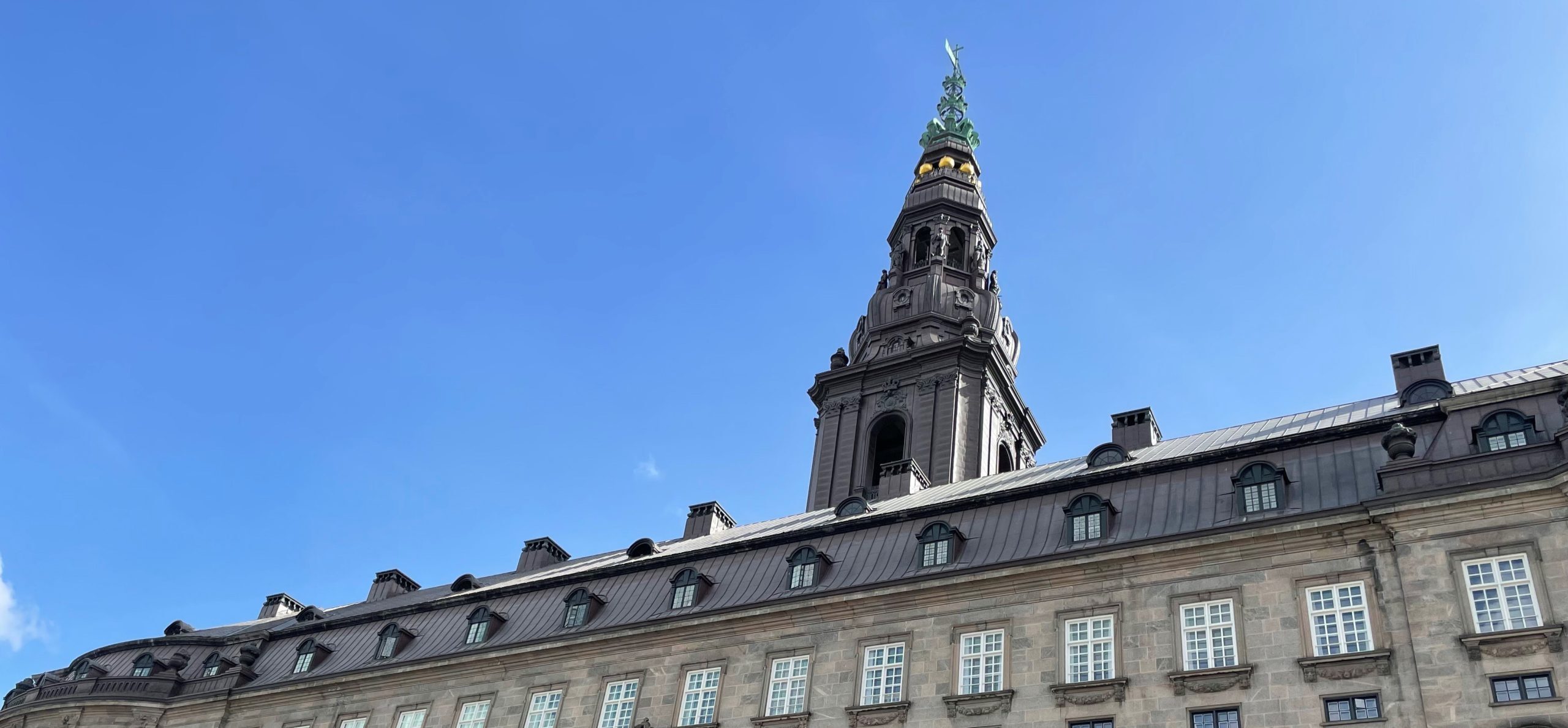 Christiansborg Slots tårn under en klar blå himmel, set fra en lav vinkel med fokus på bygningens detaljer og arkitektur.