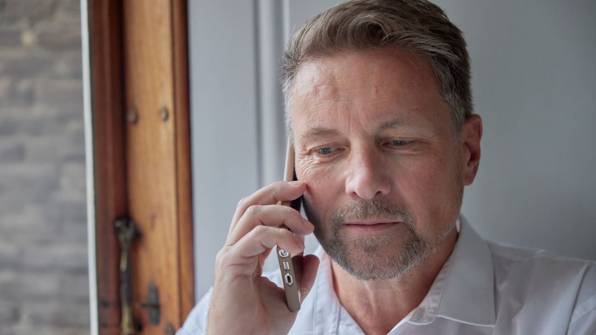 midaldrende mand med kort skæg taler i telefon og ser koncentreret ud.