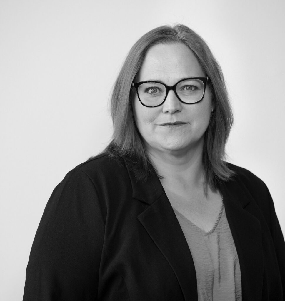 Sort-hvidt portræt af en kvinde med skulderlangt hår og briller, iført en jakke og bluse, med neutral baggrund.