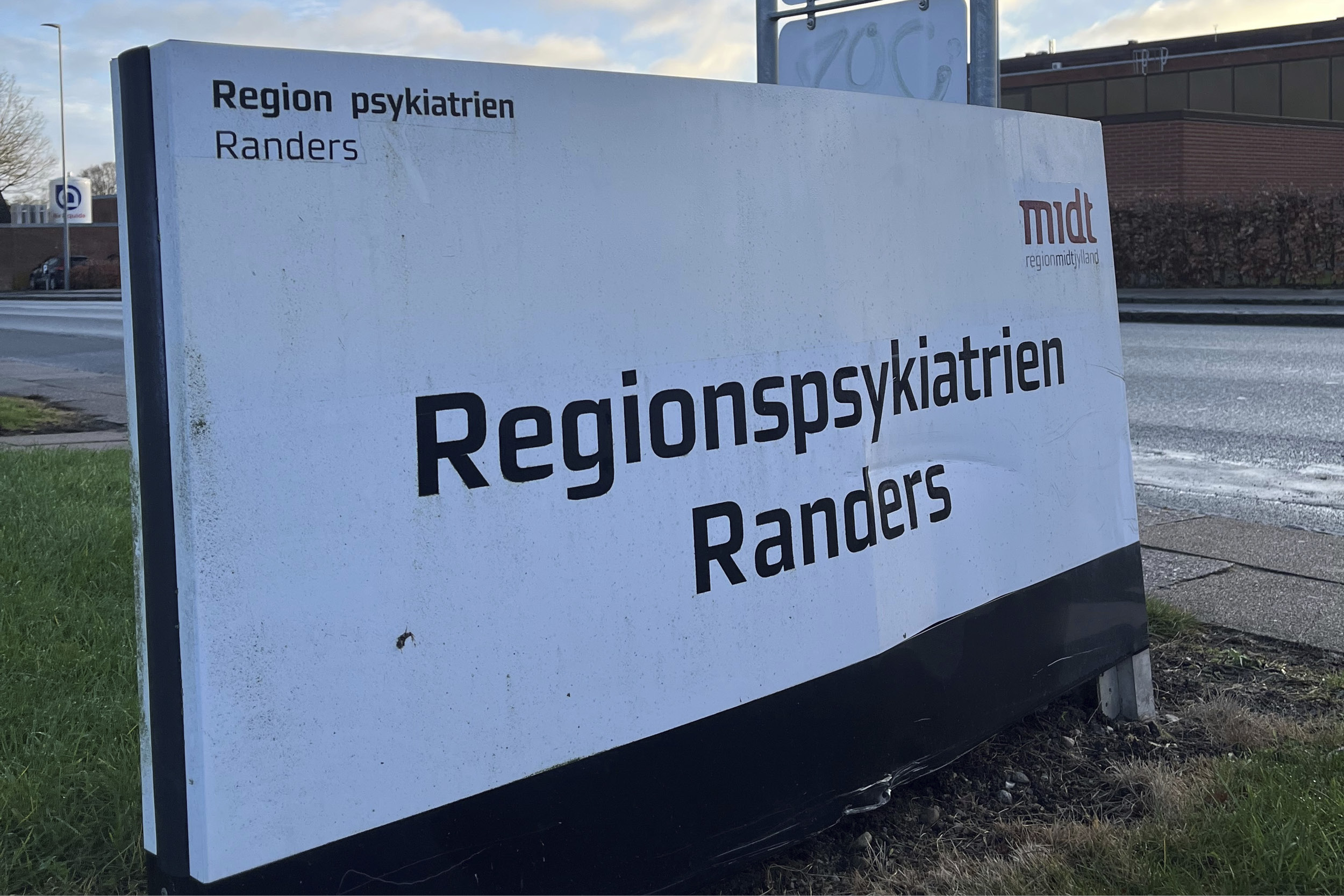 skilt med teksten "Regionspsykiatrien Randers" foran et byggeri, delvist dækket af skygge.