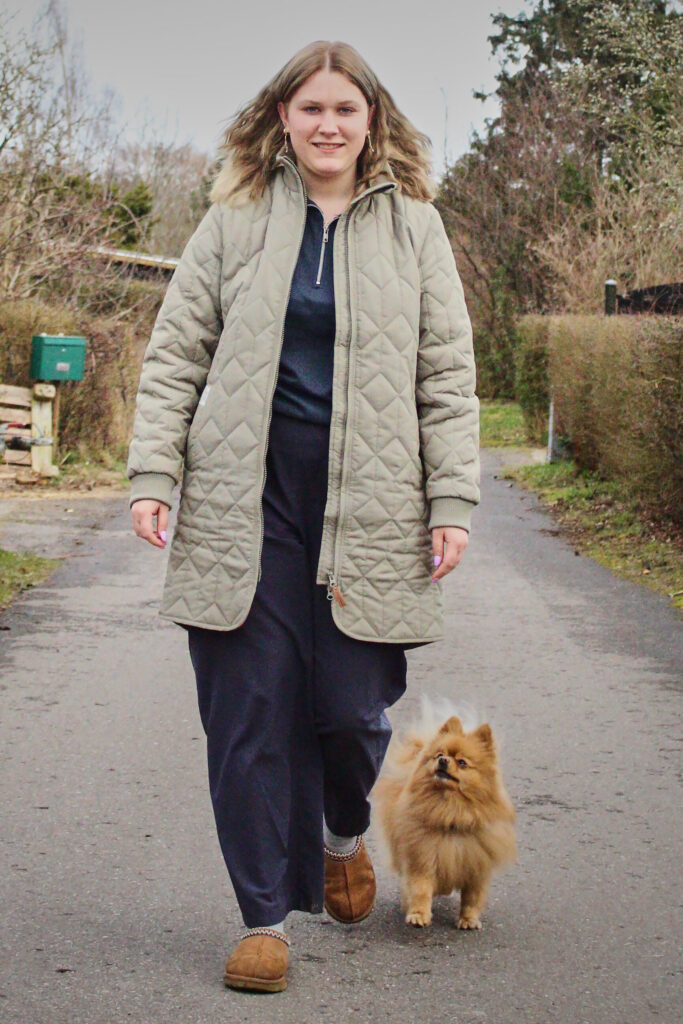 Person går på vej iført quiltet frakke sammen med en lille brun hund.