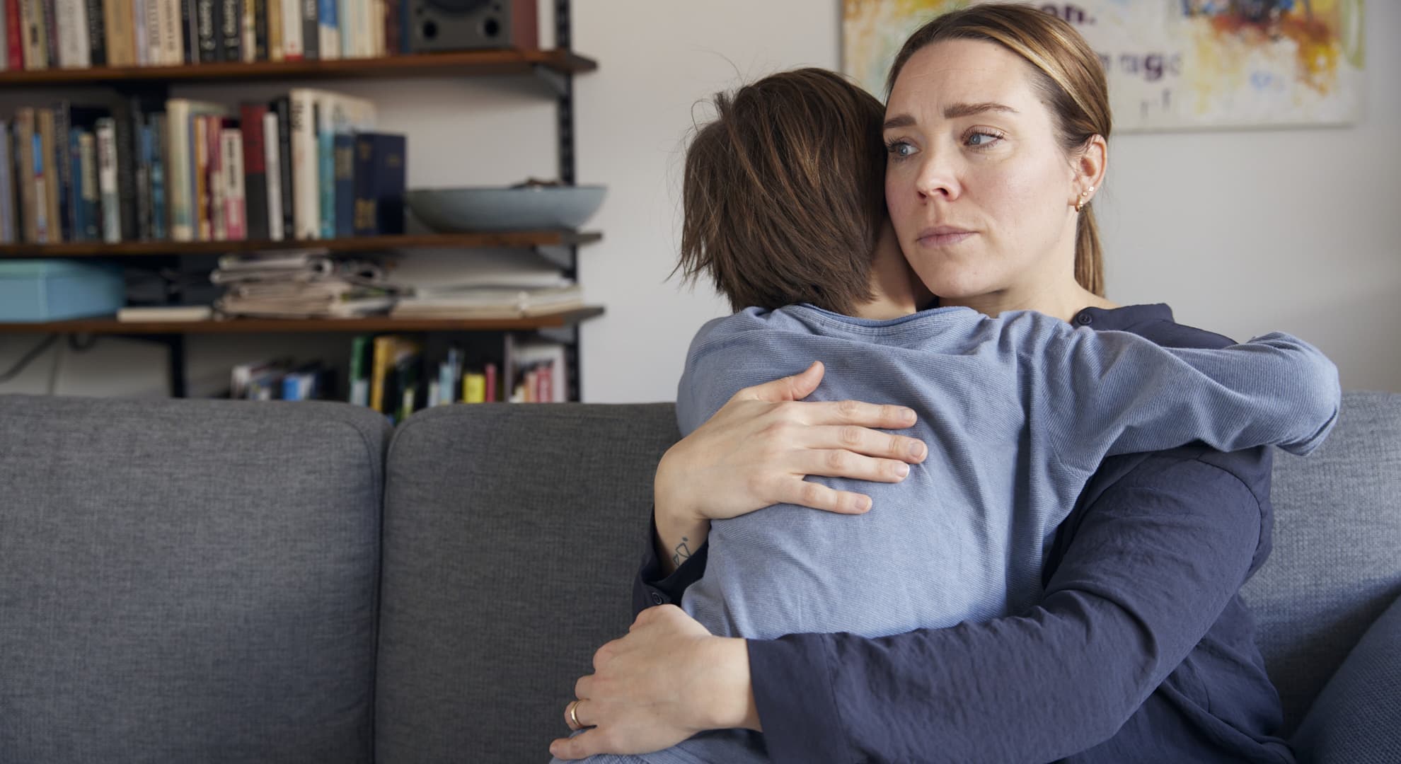 kvinde krammer et barn tæt i stuen, ser alvorlig ud og trøster barnet.