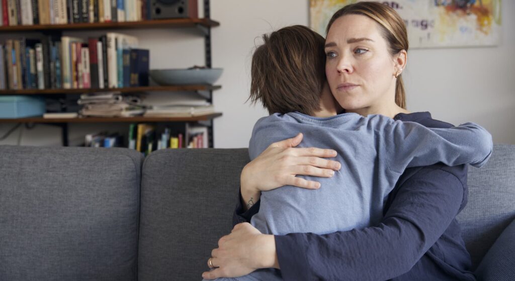 kvinde krammer et barn tæt i stuen, ser alvorlig ud og trøster barnet.