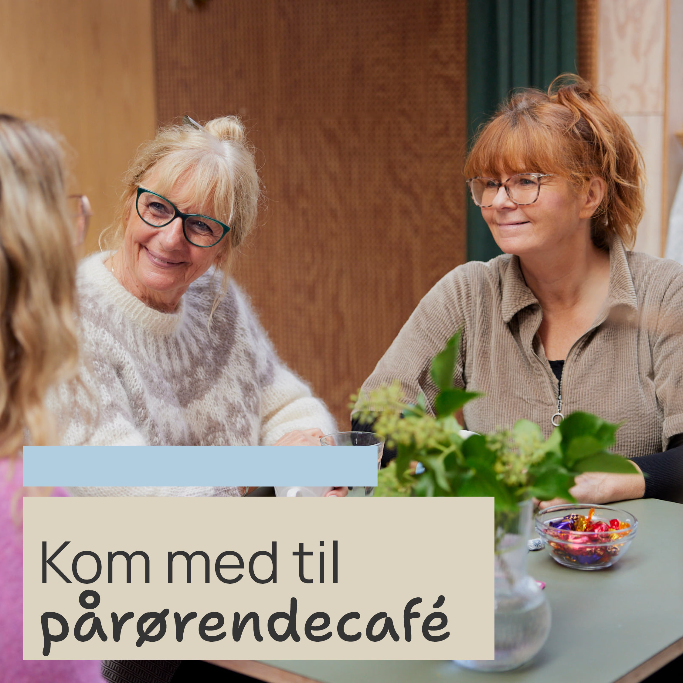 kvinder sidder og smiler ved et bord med planter og slikskål, tekst: "Kom med til pårørendecafé".