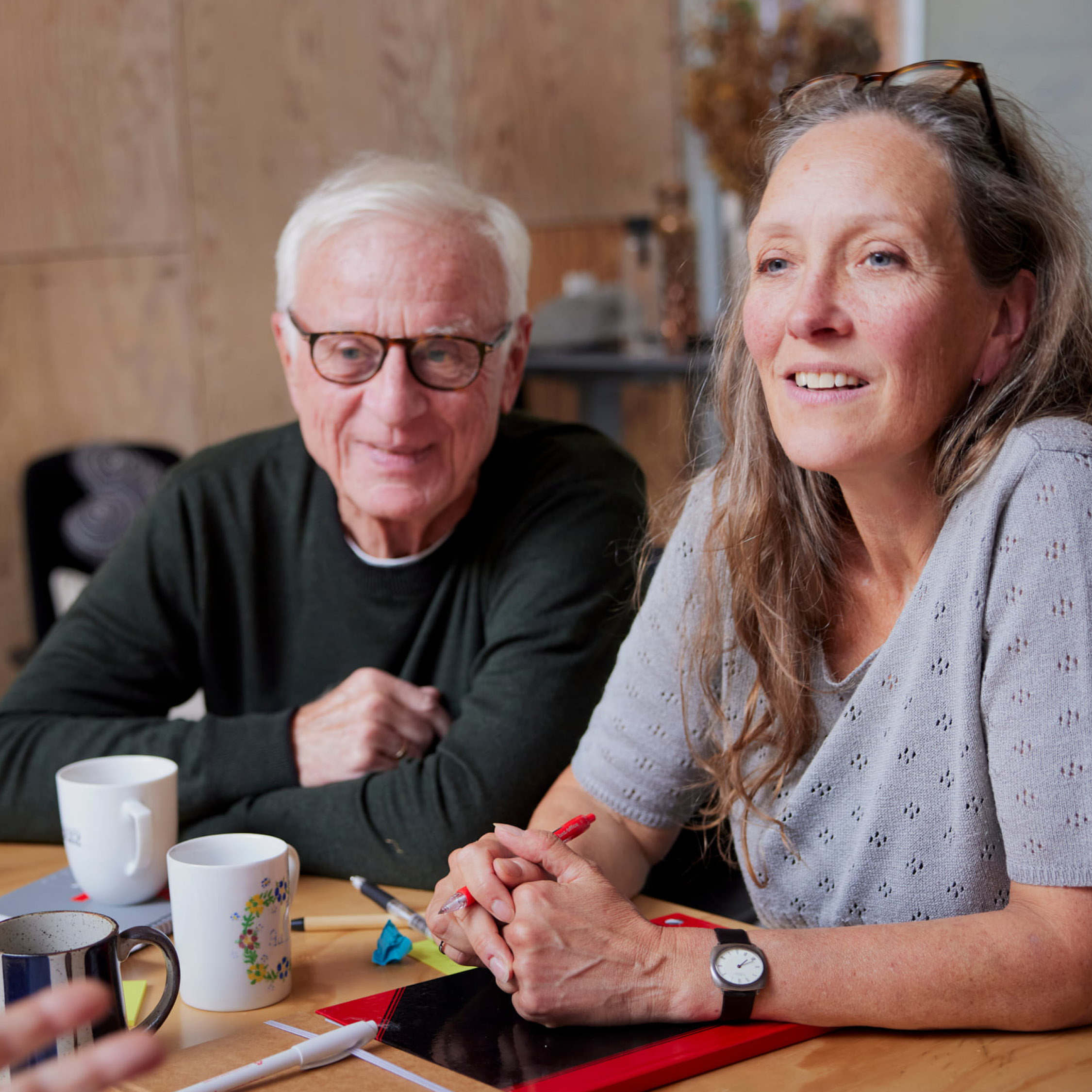 voksne personer sidder ved et bord med kaffekopper og taler sammen i et lyst rum.