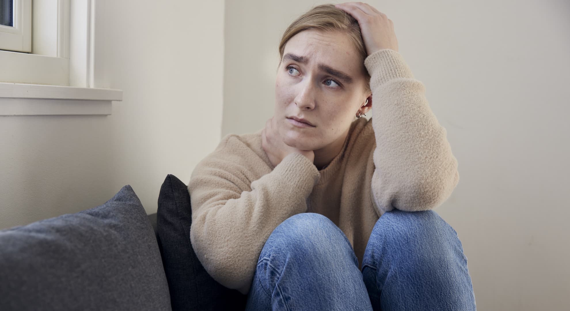 person med bekymret udtryk sidder på en sofa med én hånd i håret og ser til siden.