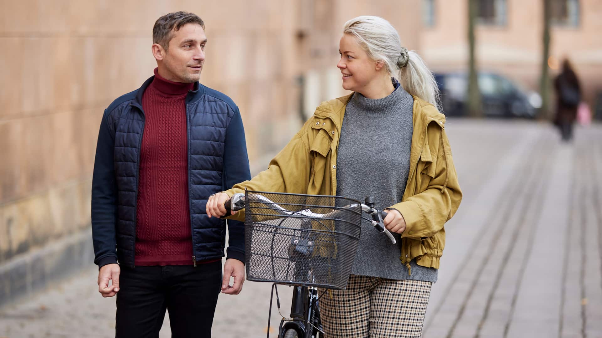 mennesker går sammen udenfor, kvinden skubber en cykel, og de smiler til hinanden på en byvej.